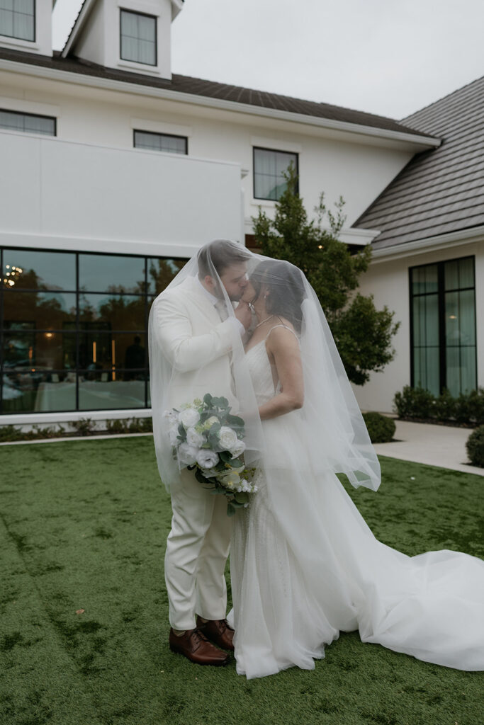 bride and groom kissing underneath veil