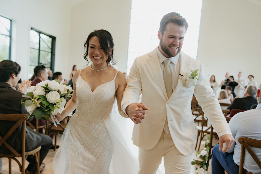 couple holding hands and smiling walking down the aisle