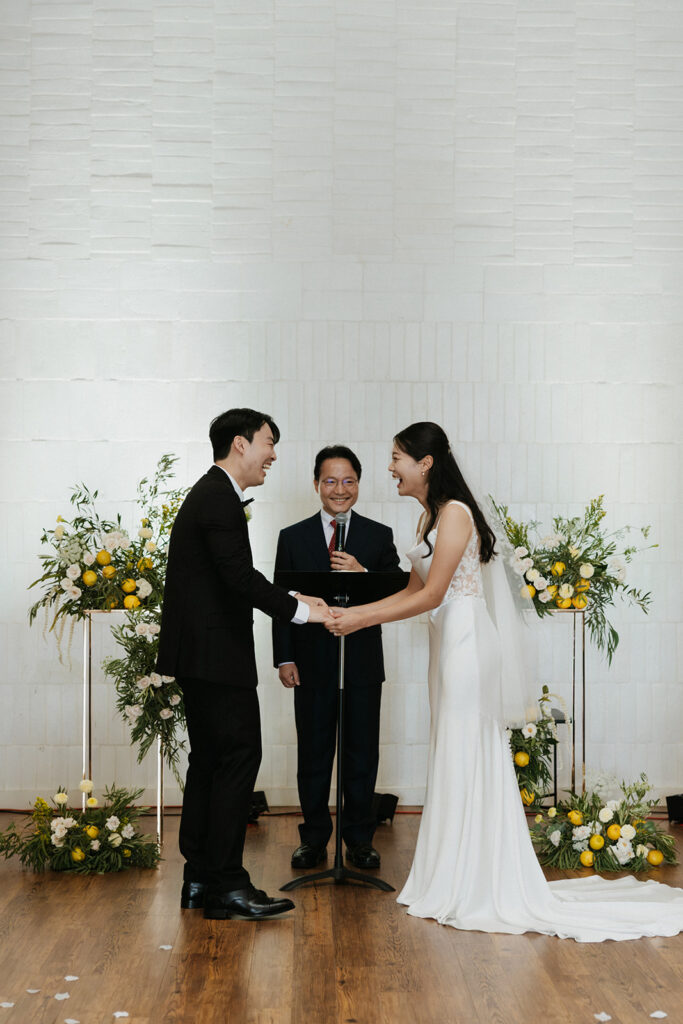 Bride and groom laughing and holding hands during theit Christ centered wedding ceremony at One Eleven East Hutto Texas.