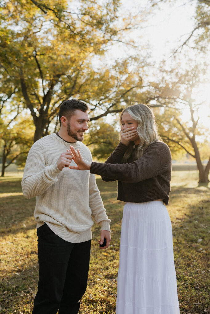 A girl with her hand to her mouth looking at her engagement ring during a surprise proposal. 