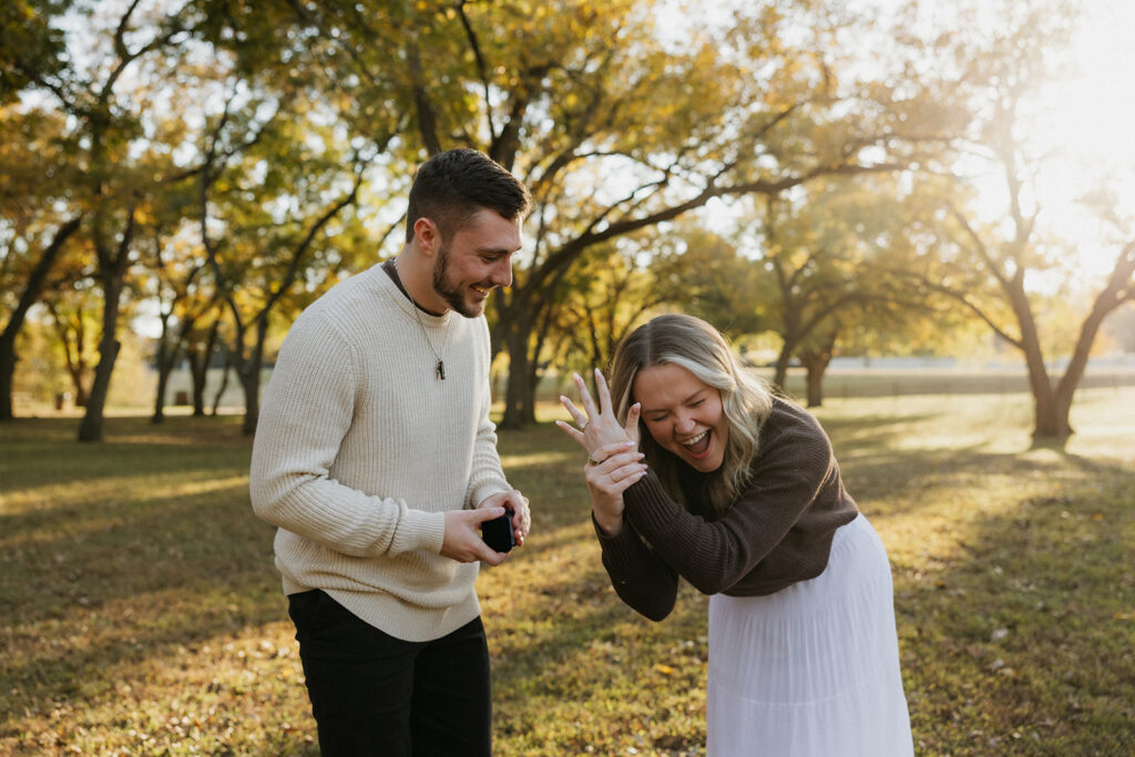 A man holding a ring box while his fiancé holds up her hand in excitement.