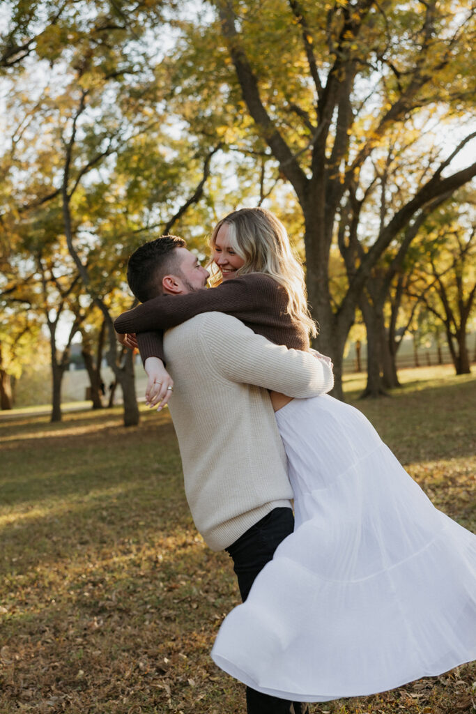A man spinning his fiancé under the trees at Elmer W. Oliver Nature Park.