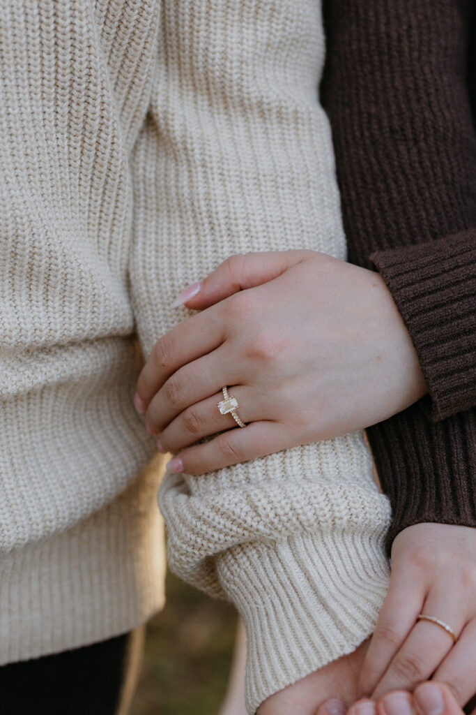 A girls hand wrapped around her fiancés arm with her engagement ring showing. 