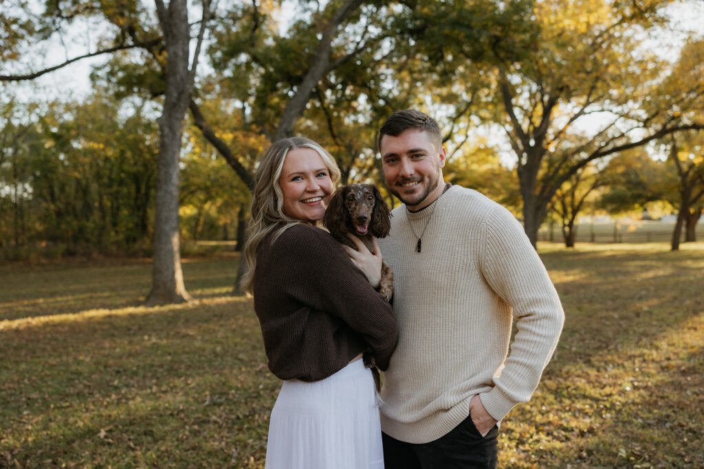 A couple holding their dog during a couples photoshoot during golden hour at Elmer W. Oliver Nature Park.