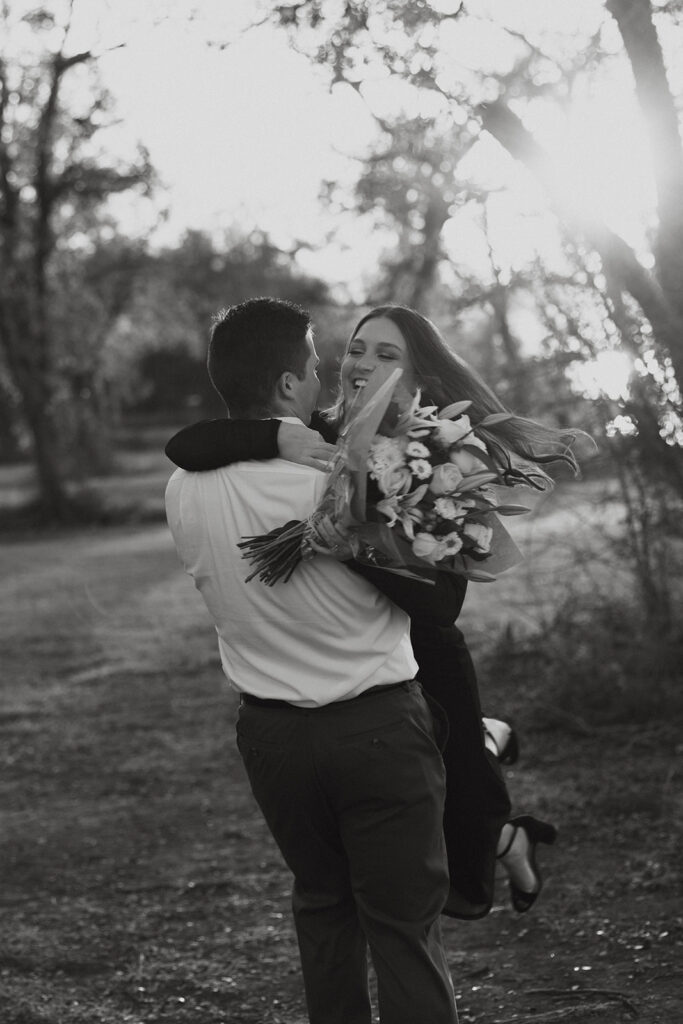 Man spinning his fiancée in his arms while she holds a bouquet of flowers.