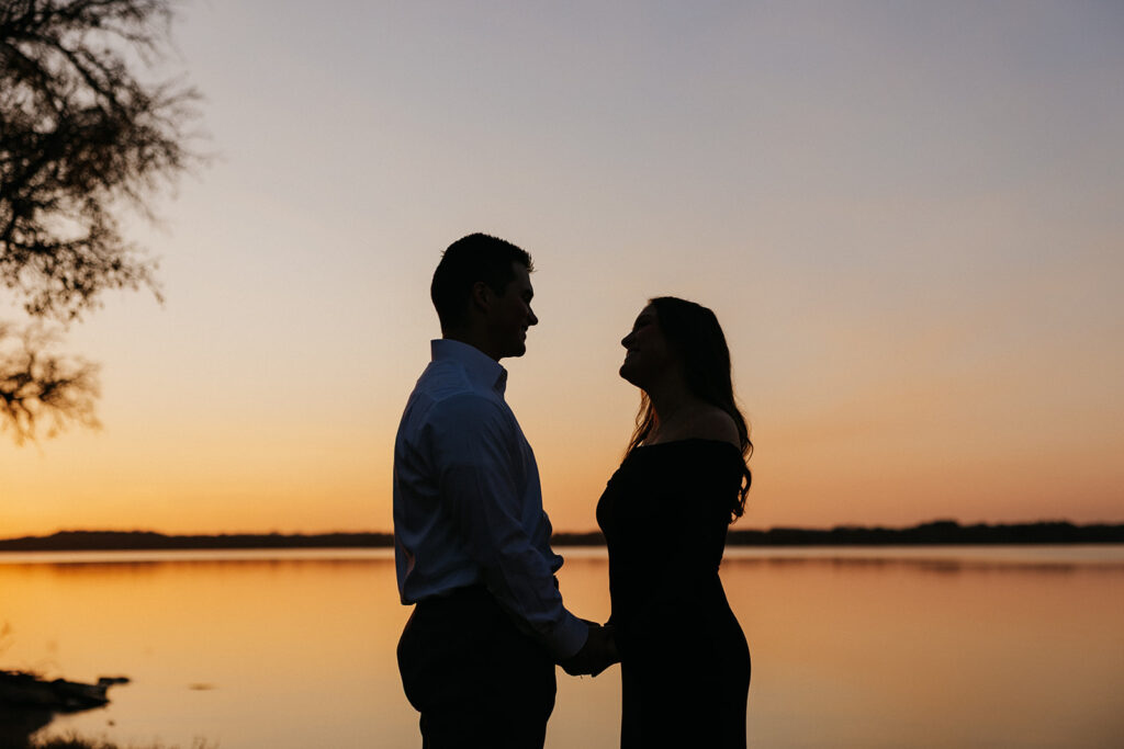 Engaged couple holding hands during sunset at Waco Lake for proposal photos.