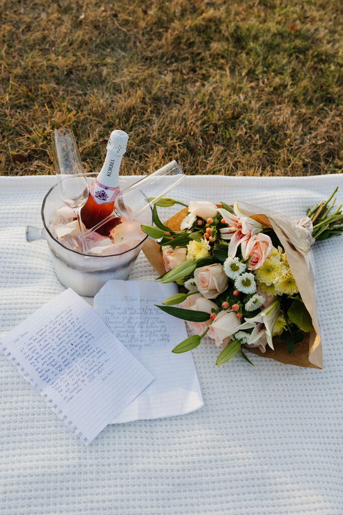 Picnic setup with love letters, flowers, and champagne. 