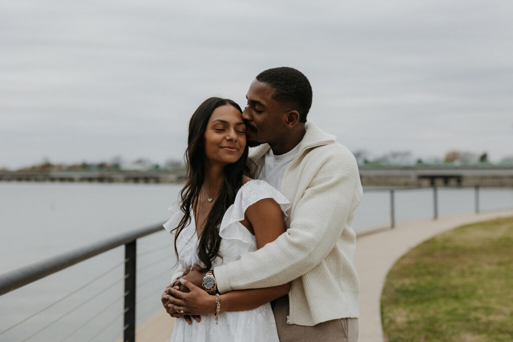A man kissing his fiancée's cheek during their romantic proposal.