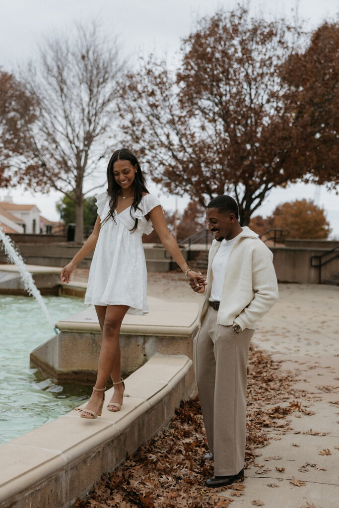 The couple smiling and walking around the fountain at The Harbor in Rockwall.