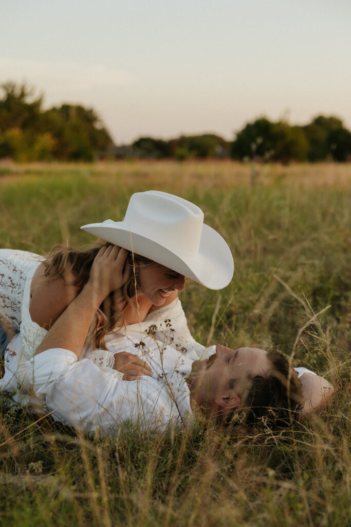 Couple playfully laying in grass, laughing together.
