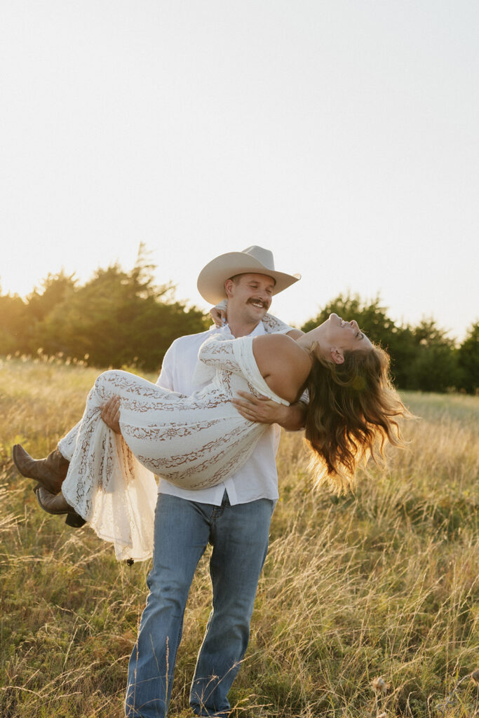 Man holding his fiancée in his arms, playfully swinging her around for summer engagement photos.