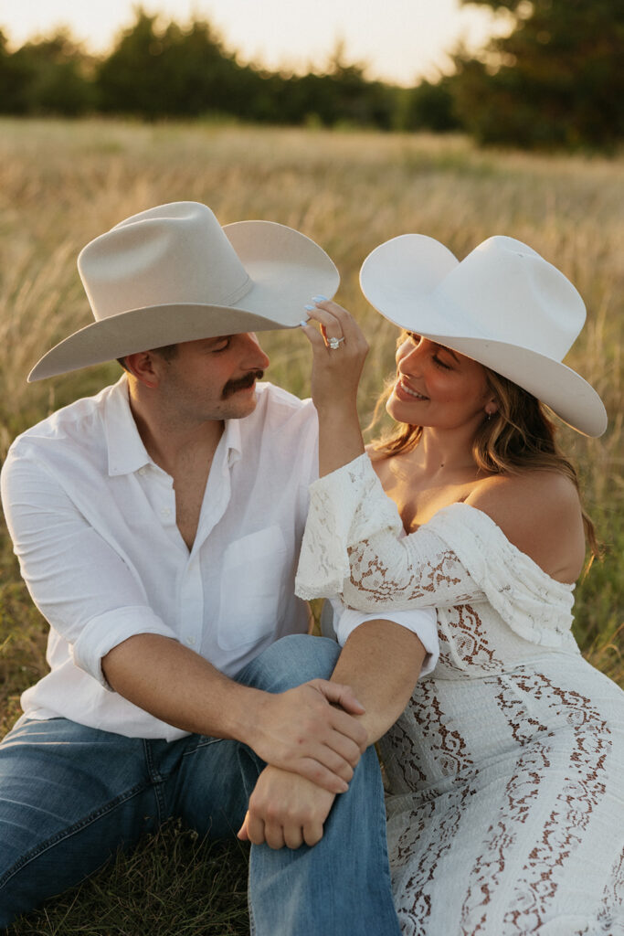 Woman adjusting the cowboy hat for her fiancé as they pose for summer engagement photos.