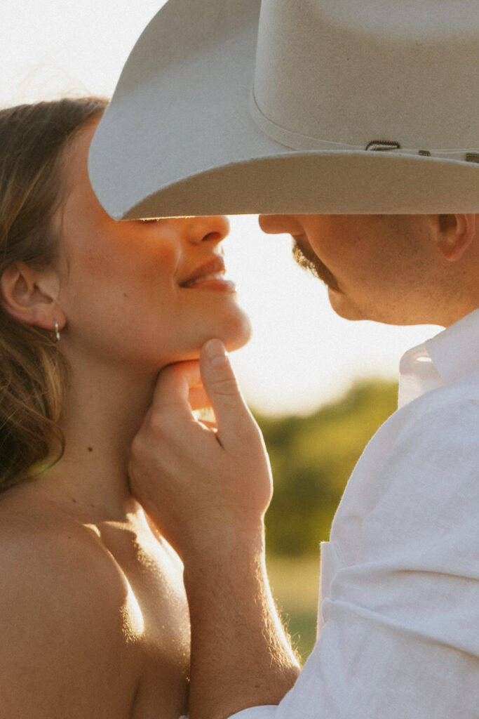 Engaged couple going in for a kiss while the sun sets behind them.