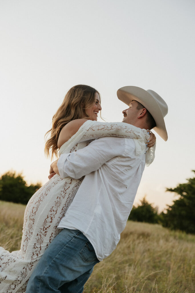 Woman with her arms around her fiancé's neck as they smile and laugh together during summer engagement photos in Dallas.