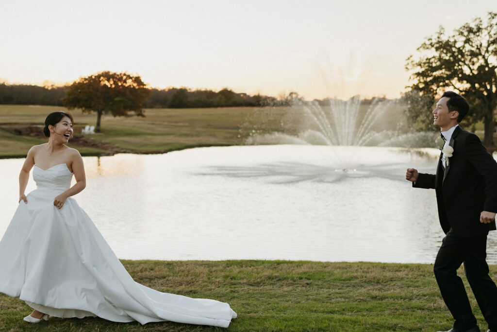 Groom playfully chasing the bride in front of a large fountain and lake at Bella Cavalli Events in Texas.