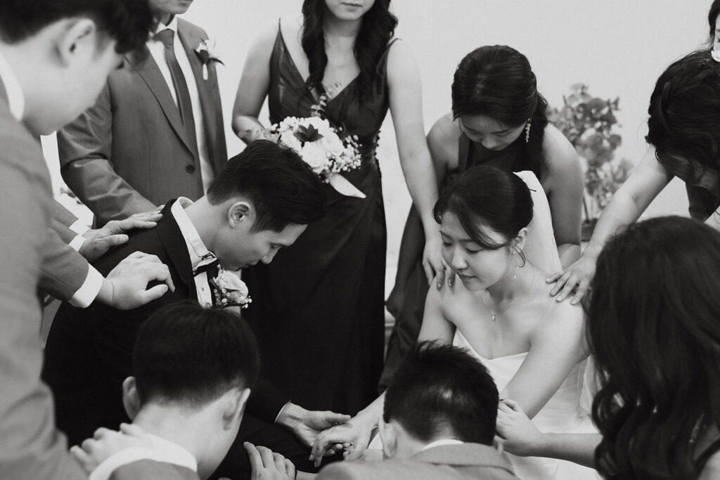Wedding party with their hands laid on the bride and groom as they pray over the couple before the wedding ceremony at Bella Cavalli Events.