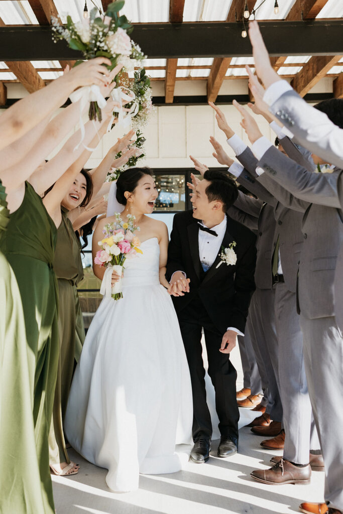Bride and groom holding hands and smiling as they walk between the wedding party with their hands in the air.