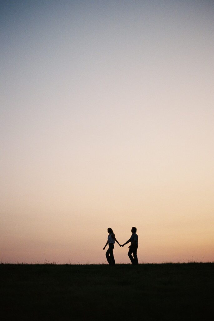 Silhouettes of a couple holding hands and walking during sunset in Rockwall, TX.