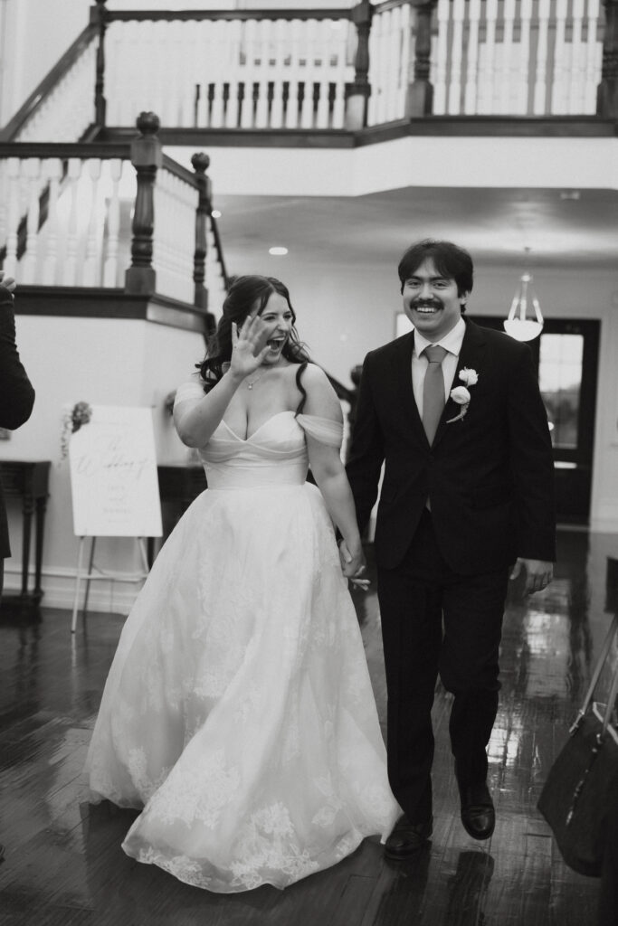 Bride and groom waving at guests as they enter the reception. 