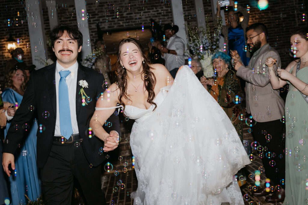 Bride and groom laughing as they exit their wedding through bubbles. 