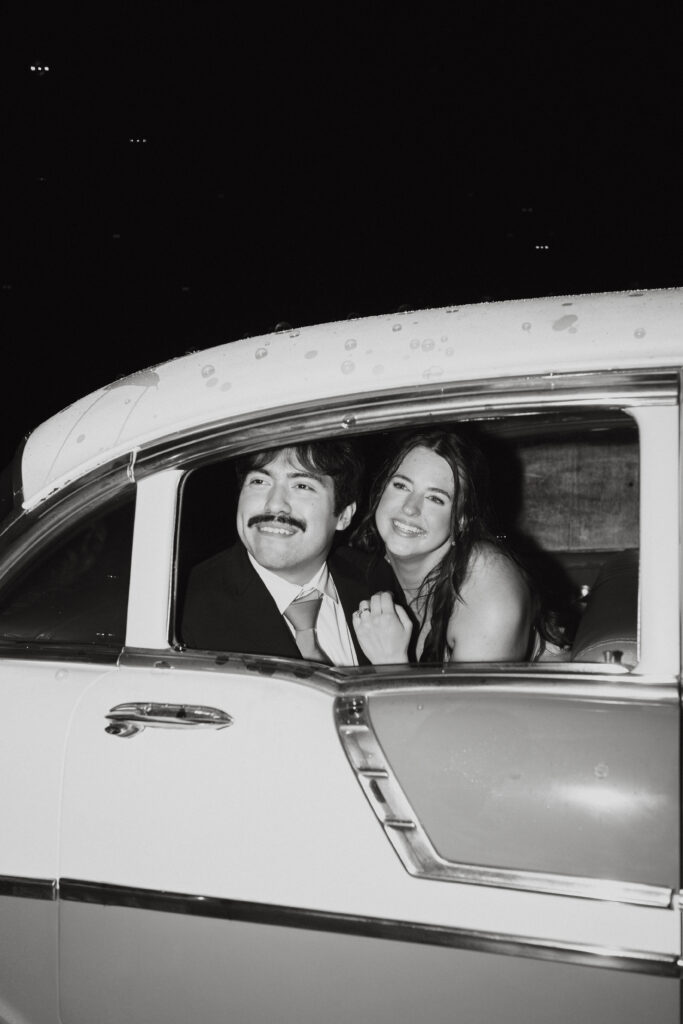 Bride and groom smiling in the backseat of a vintage car. 