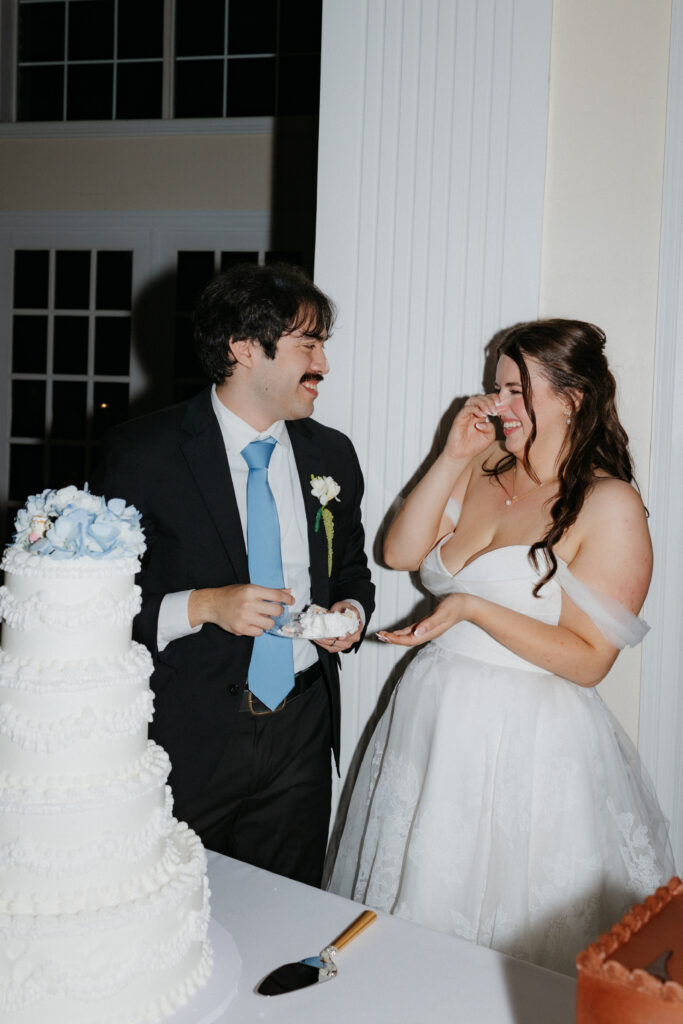 Bride and groom laughing together while eating wedding cake.