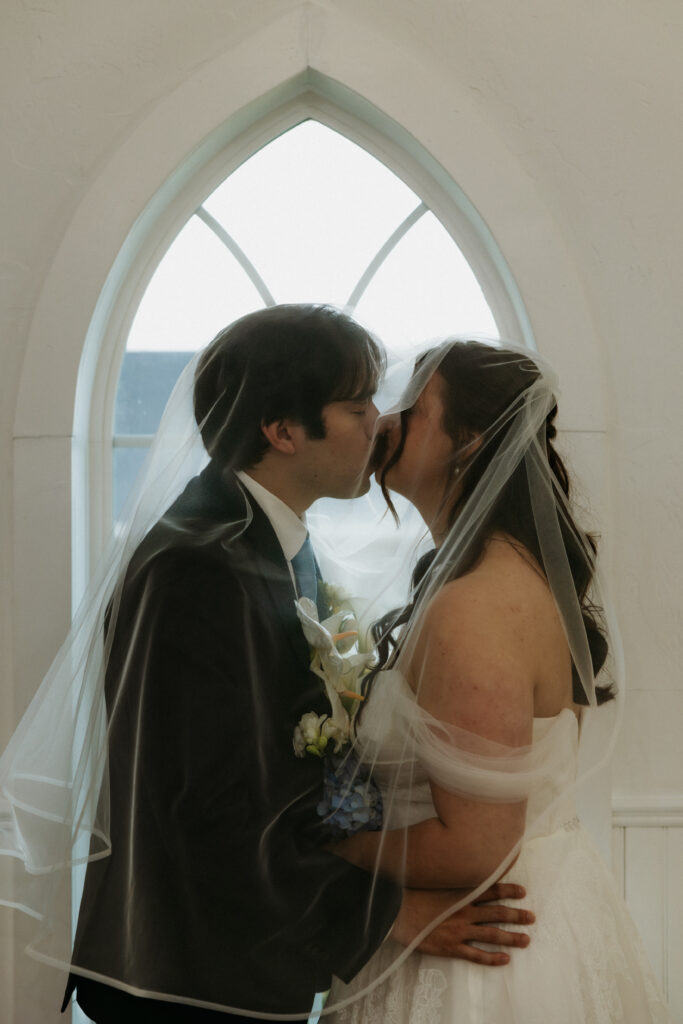 Bride and groom kissing by a window of the chapel at the Valley View Estate.