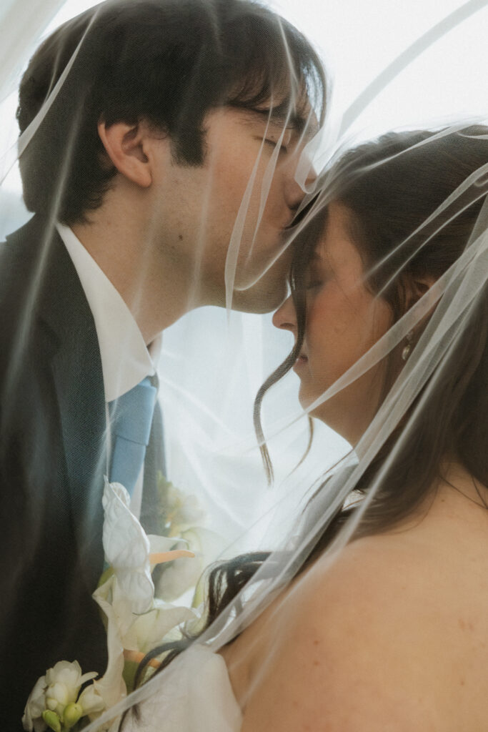 Groom kissing his bride's forehead under her veil. 