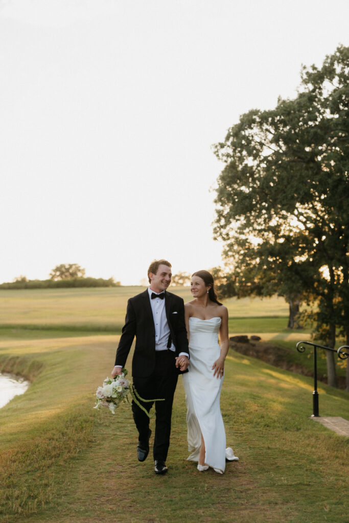 Bride and groom walking hand in hand outside.