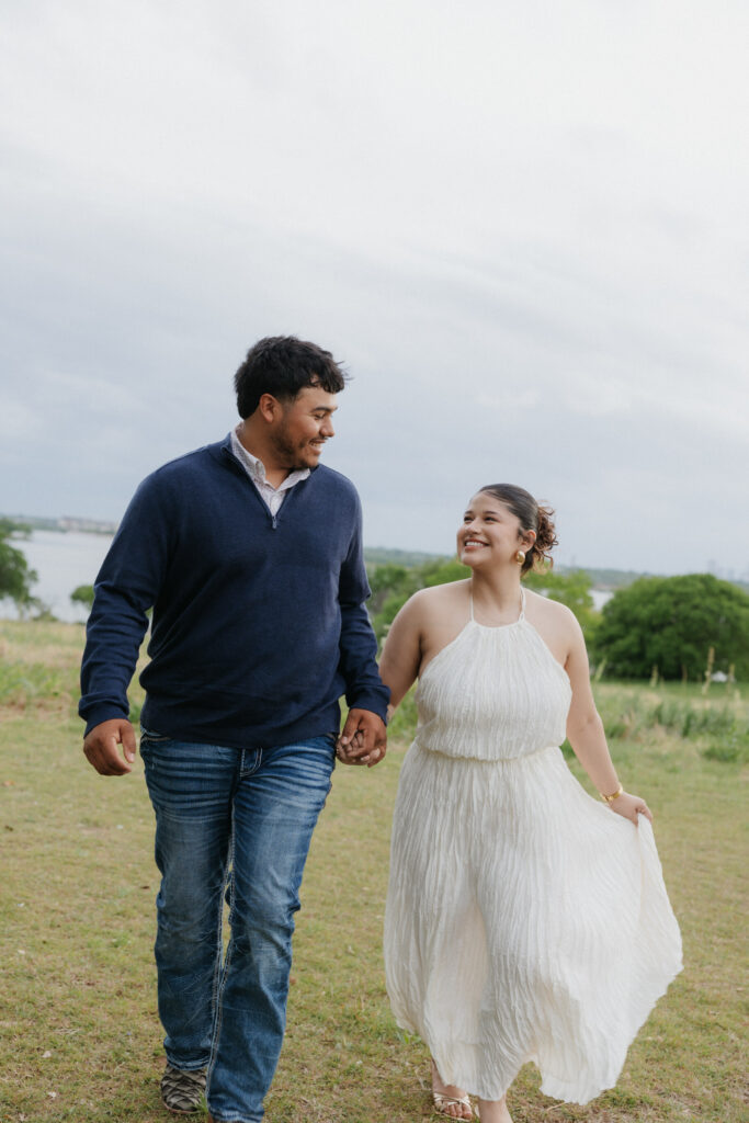 Couple holding hands and walking during their White Rock Lake engagement photos.