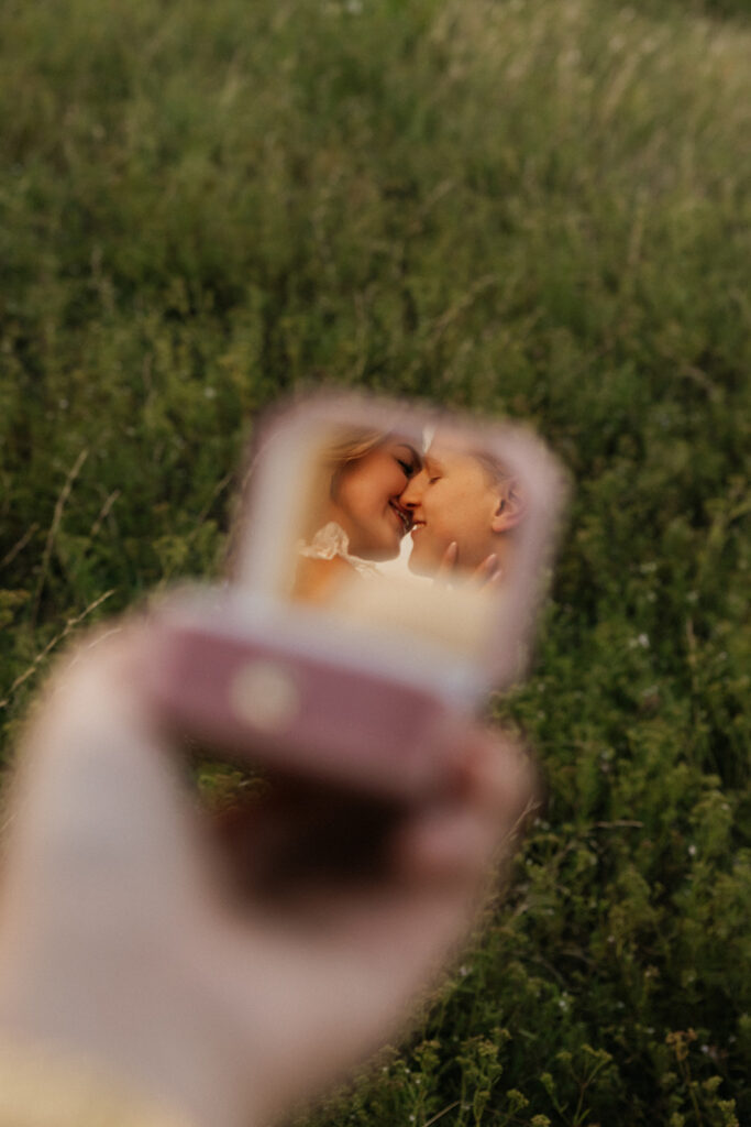 Couple about to kiss in the reflection of the mirror in the ring box, a unique outdoor proposal idea.