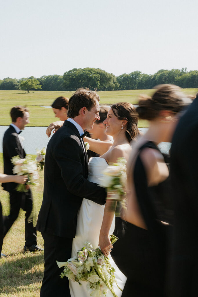 Bride and groom holding one another while the wedding party walks around them.