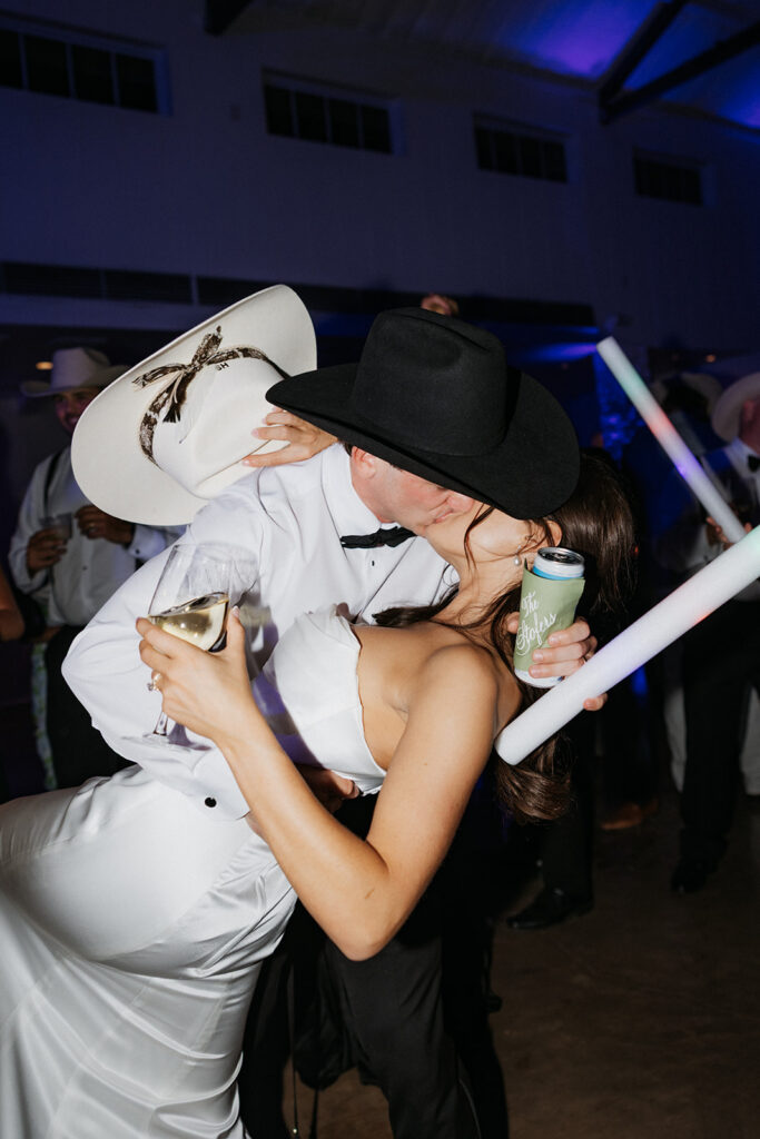 Bride and groom kissing on the dance floor while wearing western hats.