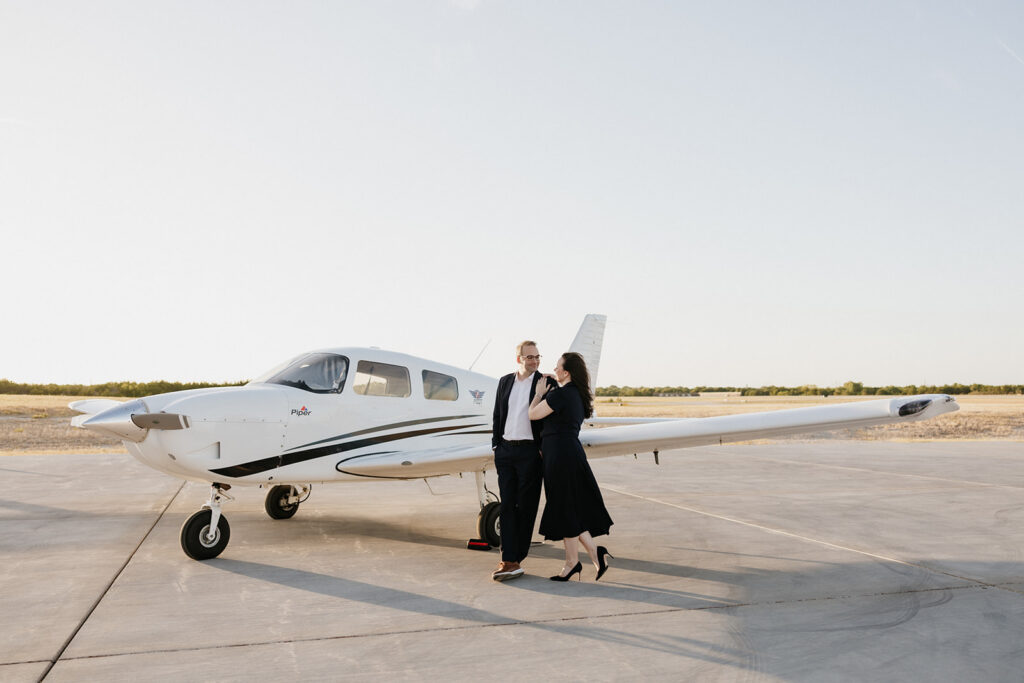 Couple holding one another while leaning against a plane during their airplane photoshoot.