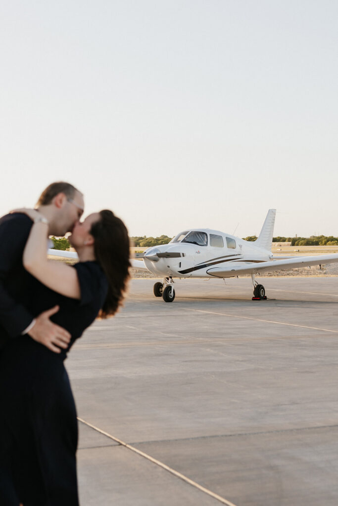 Couple kissing romantically at the airport for unique engagement photos. 