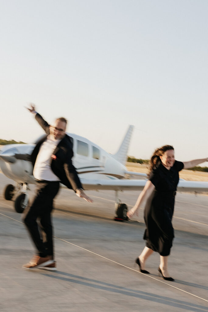 Couple with their hands in the air outside of an airplane. 