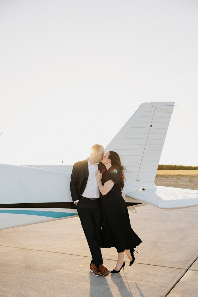 Couple kissing by a plane for unique engagement photos.