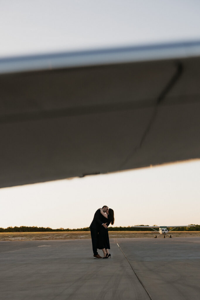 Couple kissing under the wing of an airplane during their airplane photoshoot.