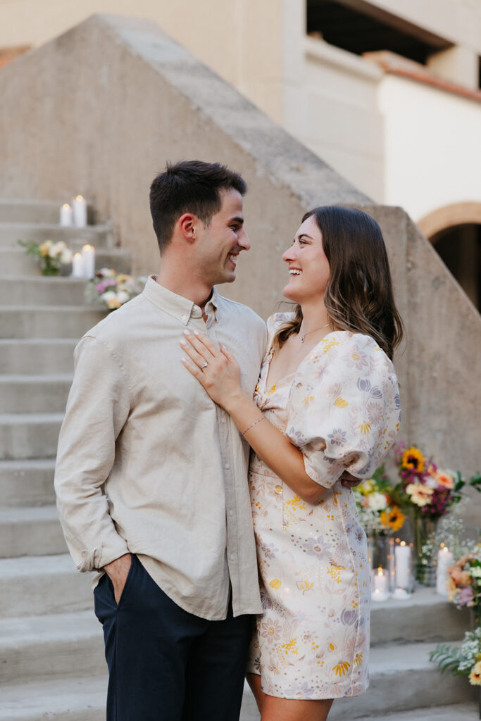 Couple smiling by a staircase lined with flowers.