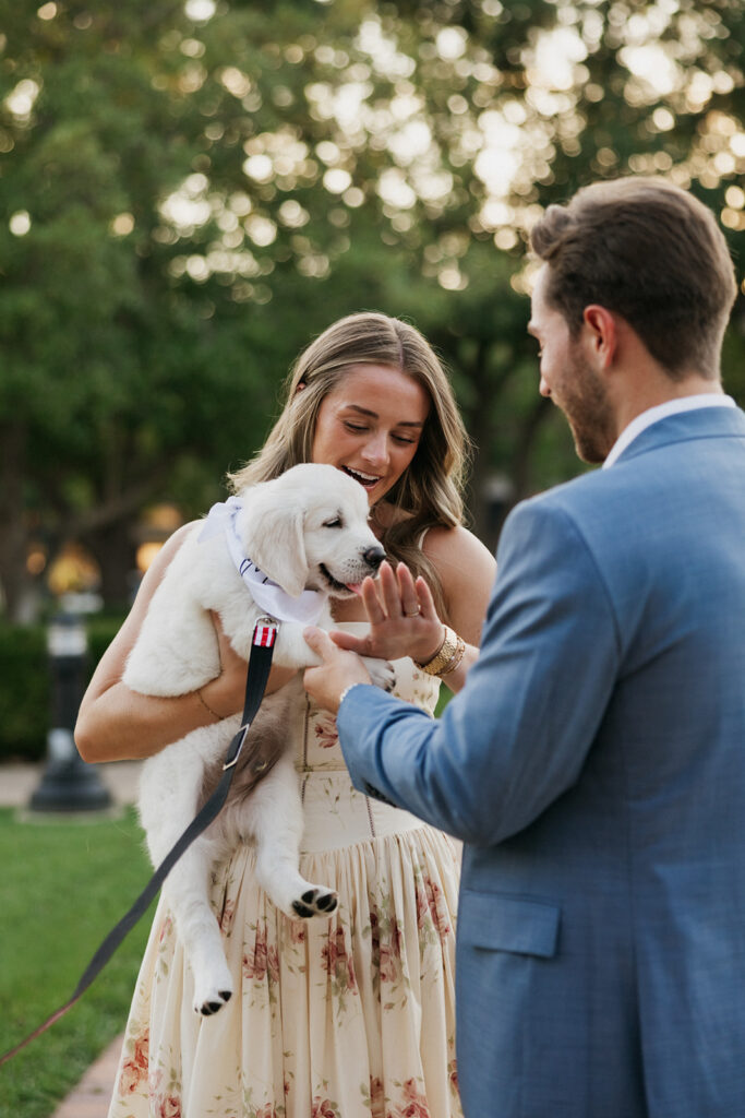 Woman holding a puppy while looking at her engagement ring.