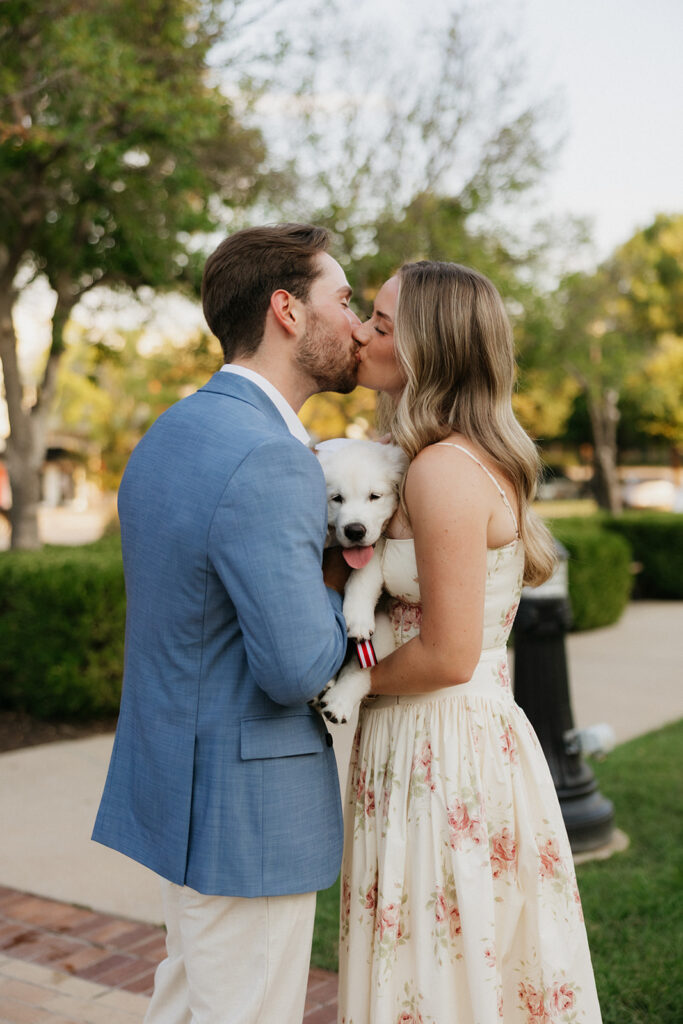 Couple kissing while holding a puppy.